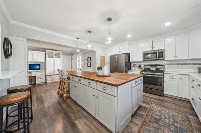 kitchen featuring appliances with stainless steel finishes, wood counters, a center island, crown molding, and backsplash