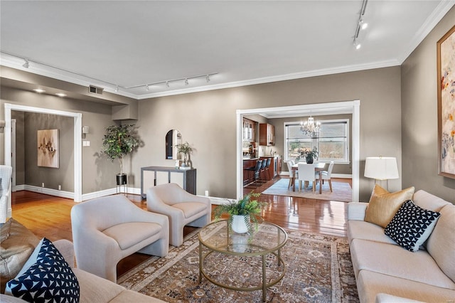 living room with rail lighting, wood finished floors, a chandelier, crown molding, and baseboards