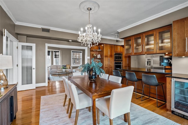 dining area featuring beverage cooler, a chandelier, ornamental molding, wood finished floors, and baseboards