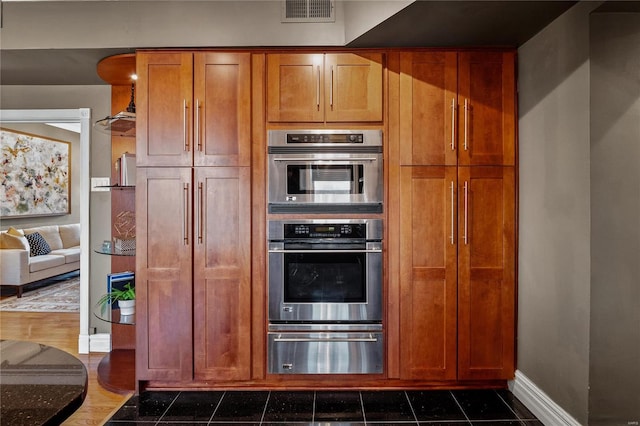 kitchen featuring a warming drawer, baseboards, brown cabinets, and double oven
