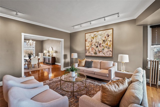 living room with track lighting, a chandelier, wood finished floors, ornamental molding, and baseboards