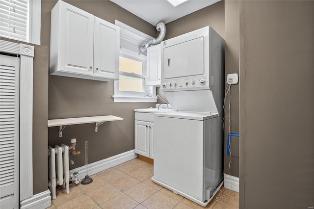 laundry area featuring estacked washer and dryer, baseboards, cabinet space, light tile patterned floors, and radiator heating unit
