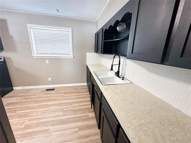 501 N Warfel St, Salem, MO 65560 - kitchen with a sink, tasteful backsplash, light wood finished floors, dark cabinetry, and baseboards