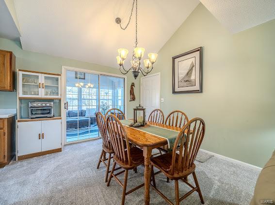 dining area featuring a chandelier, light carpet, lofted ceiling, and baseboards