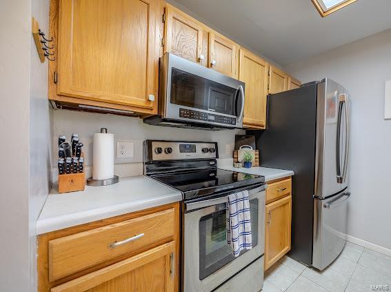 kitchen featuring stainless steel appliances, light countertops, light tile patterned flooring, and baseboards