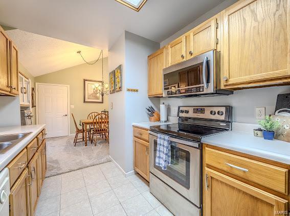 kitchen with appliances with stainless steel finishes, light carpet, light countertops, vaulted ceiling, and light brown cabinetry
