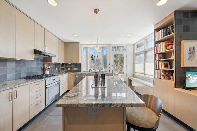 364 Mission Ct, Saint Louis, MO 63130 - kitchen with stainless steel appliances, under cabinet range hood, light tile patterned flooring, a kitchen breakfast bar, and a center island