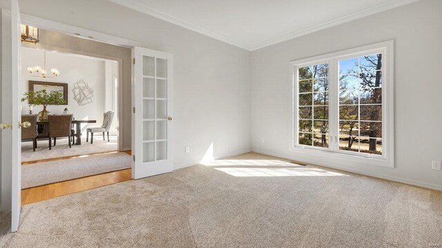 spare room featuring carpet, a chandelier, ornamental molding, baseboards, and french doors