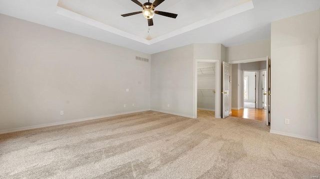 unfurnished bedroom featuring light colored carpet, a tray ceiling, a walk in closet, baseboards, and a closet