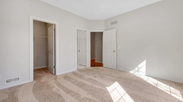 unfurnished bedroom featuring carpet flooring, a walk in closet, a closet, and baseboards