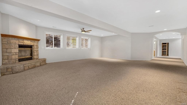 unfurnished living room featuring a fireplace, carpet floors, a ceiling fan, arched walkways, and baseboards