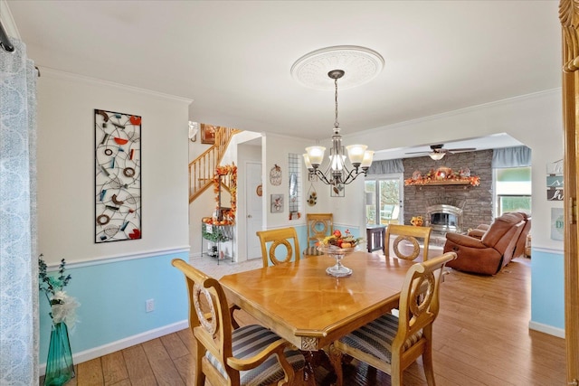 dining room featuring light wood-style flooring, stairs, a stone fireplace, crown molding, and a chandelier