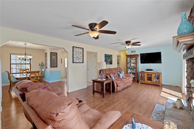 living room featuring arched walkways, light wood-style floors, a chandelier, and ceiling fan