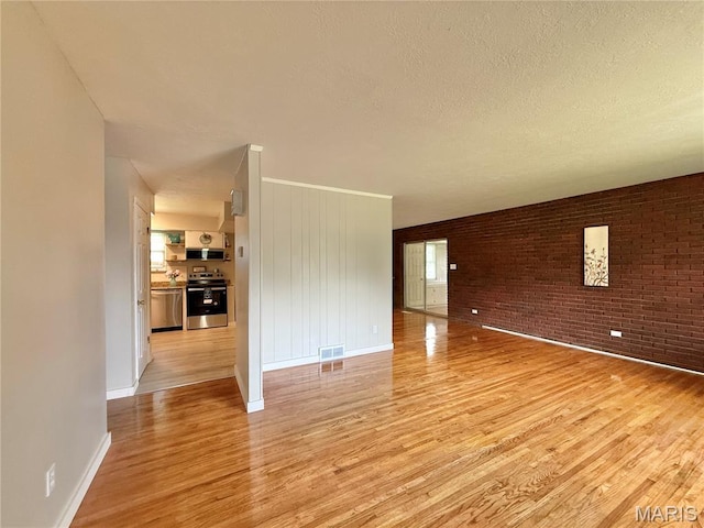 unfurnished room featuring light wood-style floors, baseboards, a textured ceiling, and brick wall
