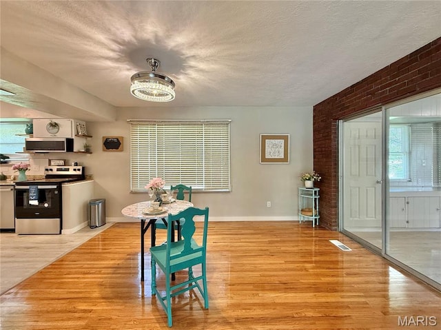 dining room with light wood-style flooring, a textured ceiling, baseboards, and brick wall
