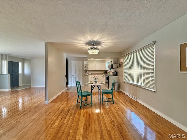 dining space with light wood finished floors, baseboards, and a textured ceiling