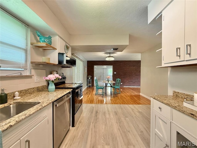 kitchen with open shelves, stainless steel appliances, white cabinets, brick wall, and a textured ceiling