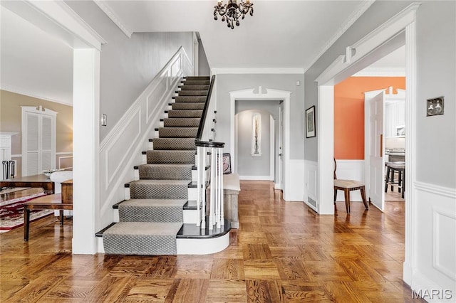 foyer with arched walkways, stairway, wainscoting, and crown molding