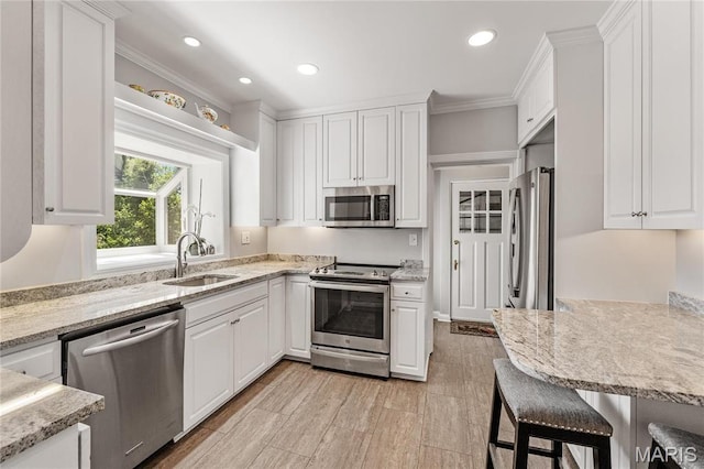 kitchen featuring stainless steel appliances, a sink, white cabinetry, recessed lighting, and light stone counters