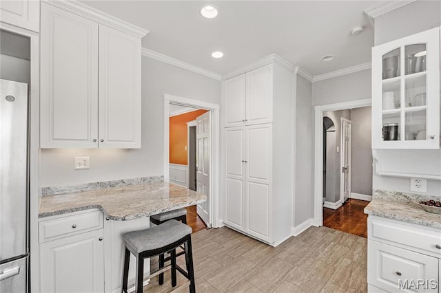 kitchen with freestanding refrigerator, crown molding, white cabinets, glass insert cabinets, and light stone countertops