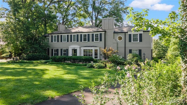 colonial inspired home featuring a chimney and a front lawn