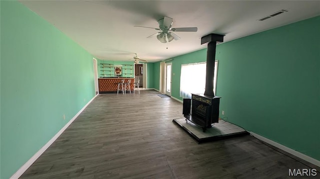 unfurnished living room with a wood stove, a ceiling fan, wood finished floors, and baseboards