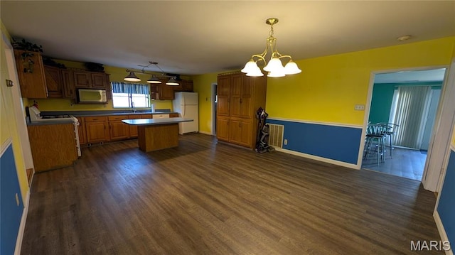 kitchen with white appliances, a kitchen island, dark wood-style flooring, a chandelier, and baseboards
