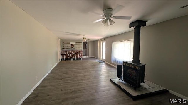 unfurnished living room with a wood stove, ceiling fan, wood finished floors, and baseboards