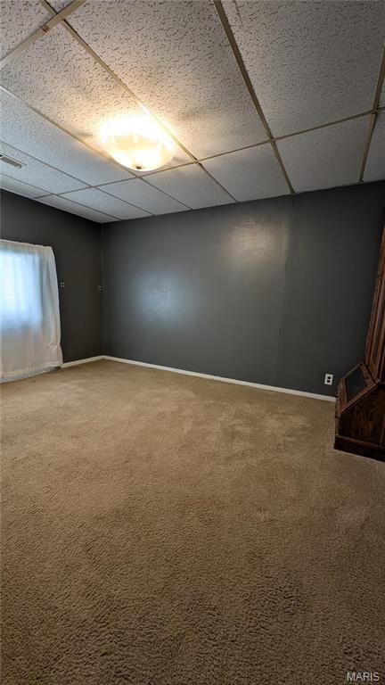 carpeted spare room with a drop ceiling and baseboards