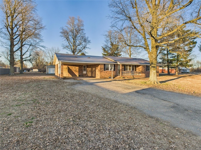 view of front of house with driveway, a porch, brick siding, a carport, and metal roof