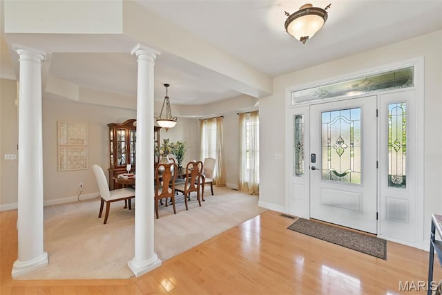 foyer entrance featuring ornate columns, plenty of natural light, and light wood-style floors