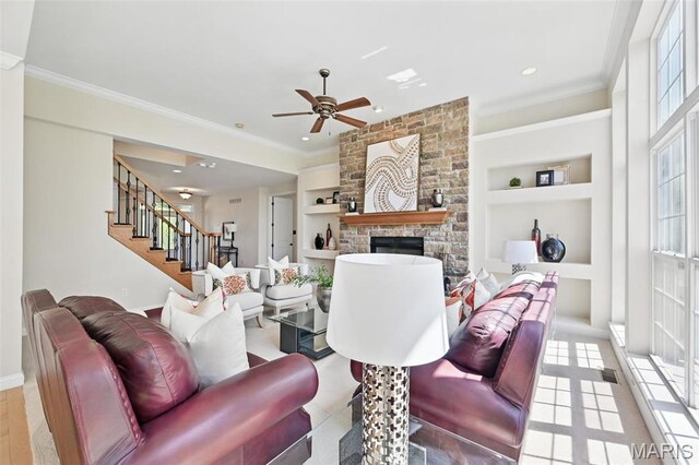 living area with built in features, ceiling fan, stairs, a fireplace, and ornamental molding
