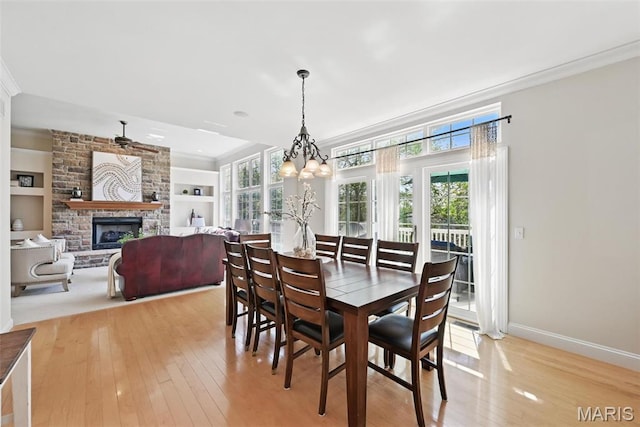 dining space with ornamental molding, light wood-style flooring, healthy amount of natural light, and a stone fireplace