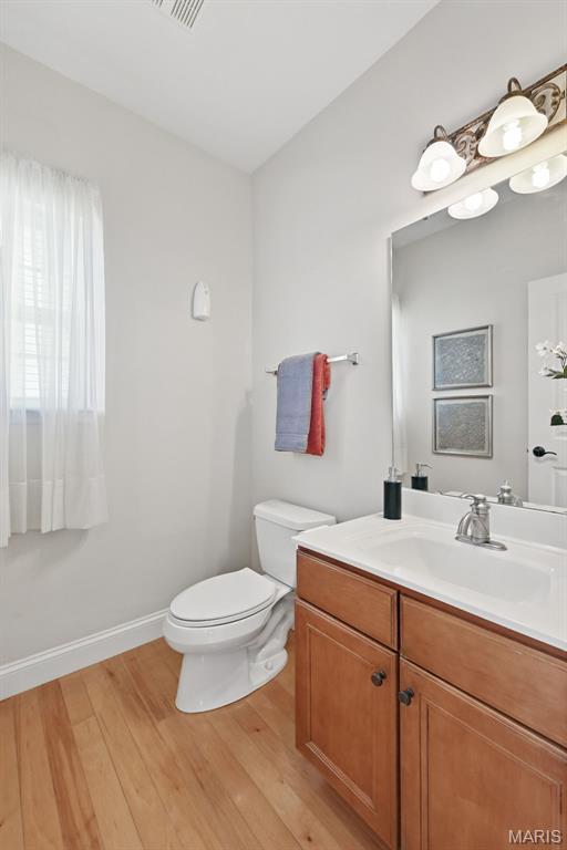 half bathroom with wood finished floors, toilet, vanity, and baseboards
