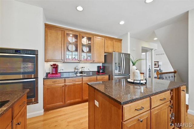 kitchen featuring appliances with stainless steel finishes, light wood-style flooring, dark stone countertops, glass insert cabinets, and recessed lighting