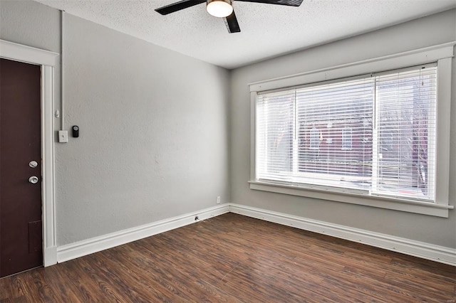 spare room featuring dark wood-style flooring, ceiling fan, baseboards, and a textured ceiling