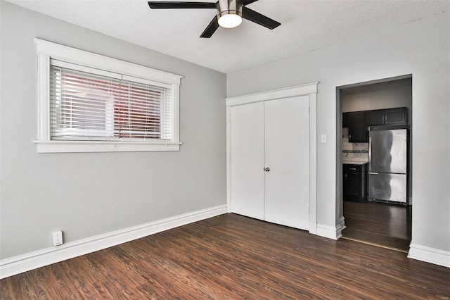 unfurnished bedroom with freestanding refrigerator, baseboards, dark wood-style floors, multiple windows, and a textured ceiling