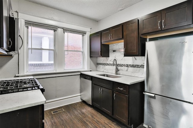 kitchen featuring appliances with stainless steel finishes, a sink, baseboards, decorative backsplash, and dark wood-style flooring