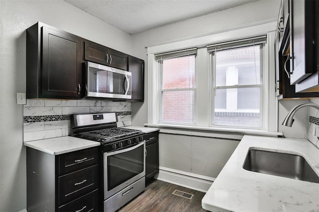 kitchen featuring appliances with stainless steel finishes, a sink, baseboards, dark wood-style floors, and tasteful backsplash