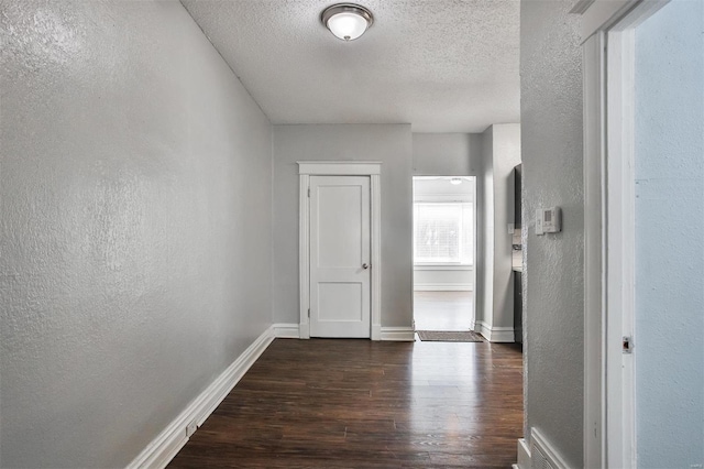 hallway with dark wood-style floors, a textured wall, baseboards, and a textured ceiling