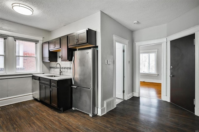 kitchen featuring appliances with stainless steel finishes, a sink, dark wood-type flooring, light countertops, and a textured ceiling