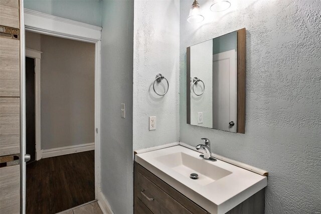 bathroom featuring baseboards, a textured wall, vanity, and wood finished floors