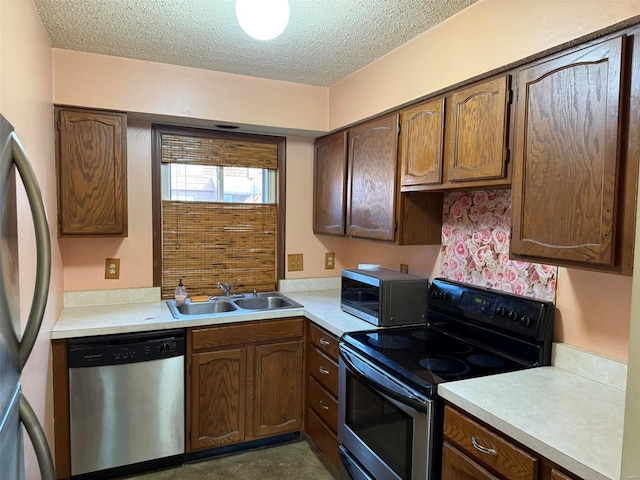 kitchen with appliances with stainless steel finishes, a textured ceiling, a sink, and light countertops