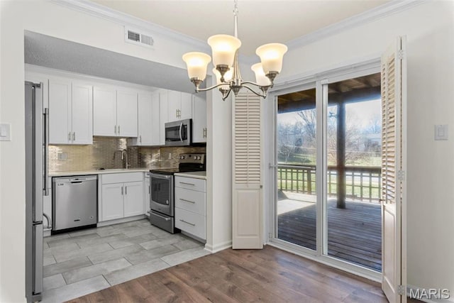 1773 High School Dr, Brentwood, MO 63144 - kitchen featuring stainless steel appliances, ornamental molding, a chandelier, white cabinetry, and backsplash