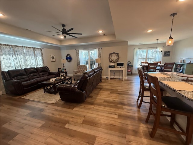 living room featuring a ceiling fan, hardwood / wood-style floors, a tray ceiling, recessed lighting, and a chandelier