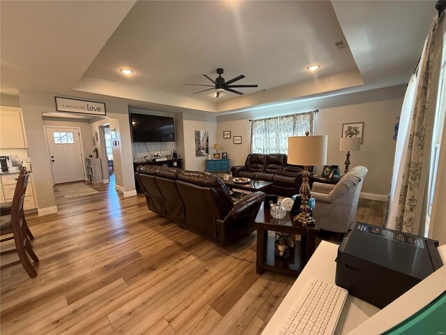 living room with a raised ceiling, a ceiling fan, light wood-style flooring, and recessed lighting