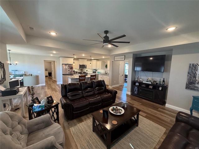 living room with baseboards, a ceiling fan, light wood finished floors, a chandelier, and recessed lighting