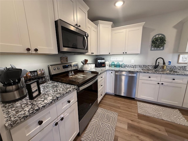 kitchen with appliances with stainless steel finishes, a sink, wood finished floors, white cabinetry, and stone countertops