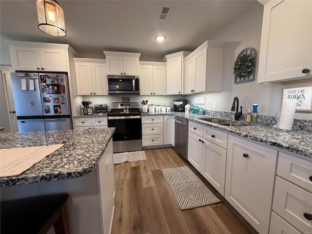 kitchen with stainless steel appliances, a sink, wood finished floors, white cabinetry, and recessed lighting
