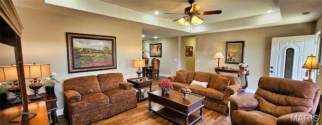 living room with wood finished floors, baseboards, ceiling fan, recessed lighting, and a raised ceiling